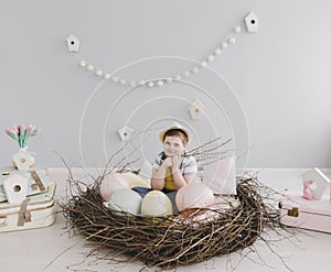 Portrait of a smiling boy in a hat. Easter composition with birds nest, easter eggs, dry willow branches.