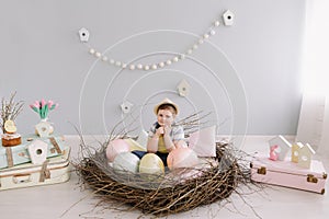 Portrait of a smiling boy in a hat. Easter composition with birds nest, easter eggs, dry willow branches.