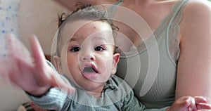 Portrait of a smiling boy sitting in his mother's arms pokes his finger at the camera and tries to take away