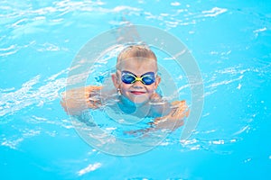 Portrait smiling boy in swimming pool, child in swimming glasses and inflatable sleeves. Summer travel hotel vacation or