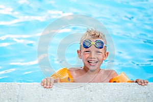 Portrait smiling boy in swimming pool, child in swimming glasses and inflatable sleeves. Summer travel hotel vacation or