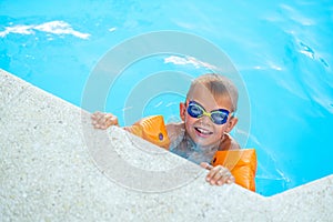 Portrait smiling boy in swimming pool, child in swimming glasses and inflatable sleeves. Summer travel hotel vacation or