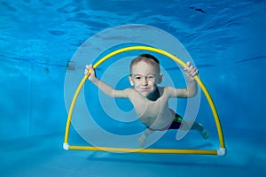 Portrait of a smiling boy underwater in a children`s pool. He swims through the Hoop, pulls out toys. Active happy child