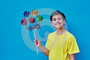 Portrait of a smiling boy in a yellow shirt holding a multi-colored pinwheel in his hand. On blue background. Copy space