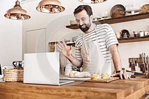 Portrait of smiling brunette man using laptop while cooking in kitchen at home