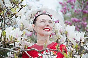 Portrait of a smiling brunette with a red lipstick lips in a red dress near a blooming magnolia