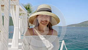 Portrait of smiling brunette woman in straw hat walking on the wooden pier at the sea beach