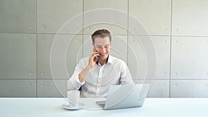 Portrait of smiling business blonde, white man, Caucasian person using laptop computer, working, and talking on smart mobile phone
