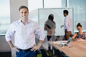 Portrait of smiling business executive standing with hands on hip in conference room