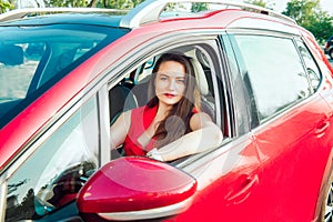 Portrait of smiling business lady, caucasian young woman driver in red clothes looking at camera and smiling while sitting behind