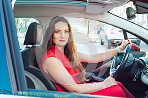 Portrait of smiling business lady, caucasian young woman driver in red summer suit looking at camera and smiling while sitting