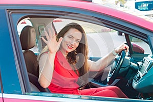 Portrait of smiling business lady, caucasian young woman driver in red summer suit looking at camera and waiving hand while