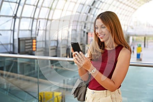 Portrait of smiling business woman browsing on mobile phone in modern city station