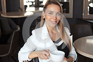 Portrait of smiling business woman drinks coffee in cafe with black interior