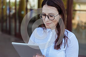 Portrait of smiling business woman using tablet pc in front of office building.