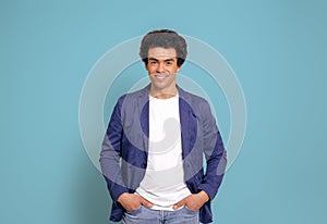 Portrait of smiling businessman with afro hairstyle and hand in pockets posing on blue background