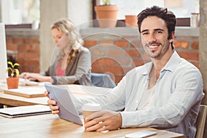 Portrait of smiling businessman holding digital tablet and coffee in office