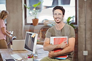 Portrait of smiling businessman holding files and folders in creative office