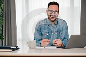 Portrait of smiling businessman with laptop and diary sitting at office desk