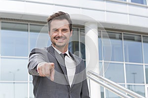 Portrait of smiling businessman pointing at you outside office building