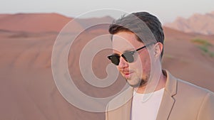 Portrait smiling businessman in sunglasses enjoying sunset in red desert in UAE.
