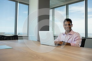 Portrait of smiling businessman using laptop in conference room