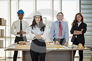 Portrait of smiling businesswoman engineer wearing helmet and diversity team colleague with architect construction model and