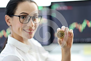 Portrait of smiling businesswoman in glasses holding golden bitcoin