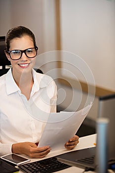 Portrait of smiling businesswoman holding documets at desk