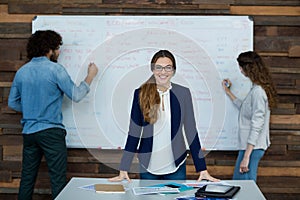 Portrait of smiling Businesswoman leaning on table while colleague working in background