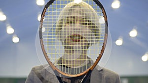 Portrait of smiling businesswoman with red lips looks through tennis racket