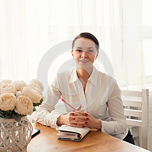 Portrait of a smiling businesswoman sitting at a table with a notebook and a pen photo