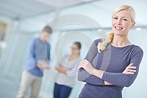 Portrait of a smiling businesswoman standing with her arms crossed and looking at the camera while her colleagues work