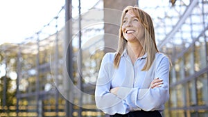 Portrait Of Smiling Businesswoman Standing Outside Modern Office Building With Folded Arms