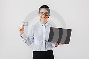 Portrait of smiling businesswoman wearing eyeglasses holding silver laptop and credit card in the office, isolated over white