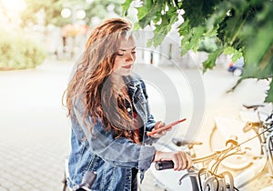 Portrait of smiling at camera red curled hair caucasian teen girl unlocking bike at Bicycle sharing point using the modern