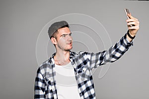 Portrait of a smiling casual man taking selfie over gray background