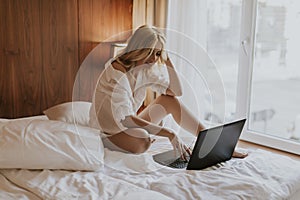 Smiling casual young woman using laptop in bed at home