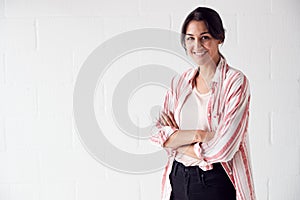 Portrait Of Smiling Casually Dressed Woman Standing Against White Brick Studio Wall