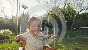 Portrait of smiling caucasian baby having fun on a swing, looking at flying soap bubbles. Slow motion. The concept