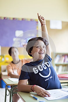 Portrait of smiling caucasian child with raised hand in class. Primary education