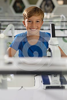 Portrait of smiling caucasian elementary schoolboy sitting at desk in science laboratory