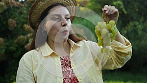 Portrait of smiling Caucasian woman eating sweet white grape healthy food outdoors. Young woman eating grapes. People