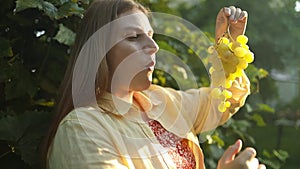 Portrait of smiling Caucasian woman eating sweet white grape healthy food outdoors. Young woman eating grapes. People