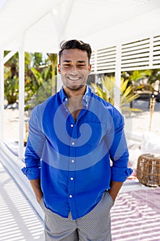 Portrait of smiling caucasian young man with hands in pockets standing at tourist resort, copy space