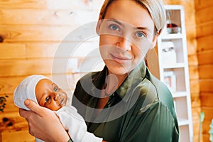 Portrait of smiling caucasian young woman holding newborn african american baby doll in her arms and looking at camera, indoors