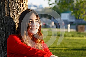 Portrait of smiling cheerful young Asian woman leaning against tree