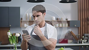 Portrait of smiling chef man looking recipe on mobile phone at home kitchen.