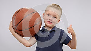 Portrait of smiling child boy showing thumb up with basketball ball in hands.