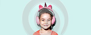 Portrait of smiling child girl listening the music with headphones on background of aqua menthe color. Panoramic banner view.